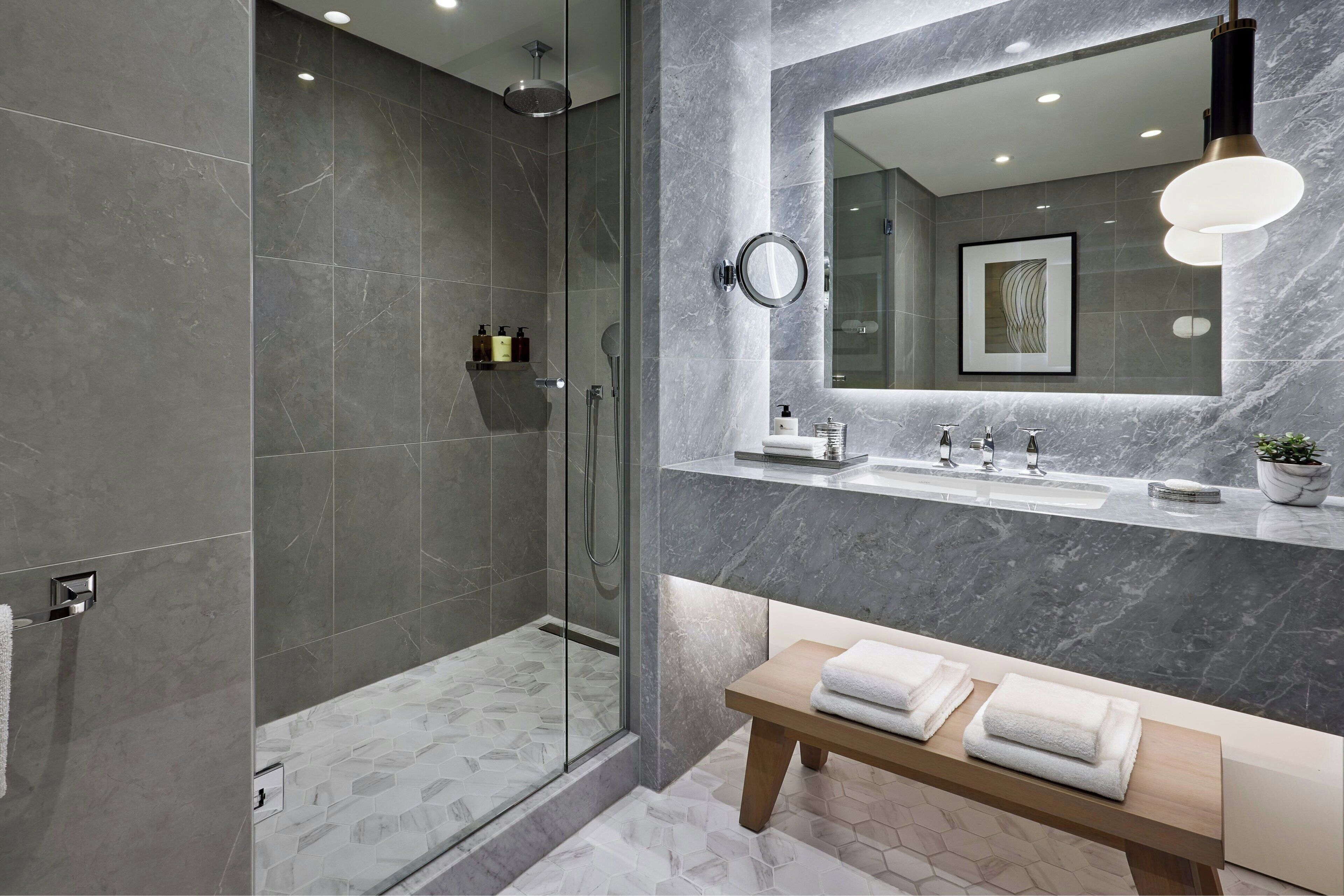 Une salle de bain moderne avec une douche à parois de verre, un meuble-lavabo avec un miroir et un banc avec des serviettes.
