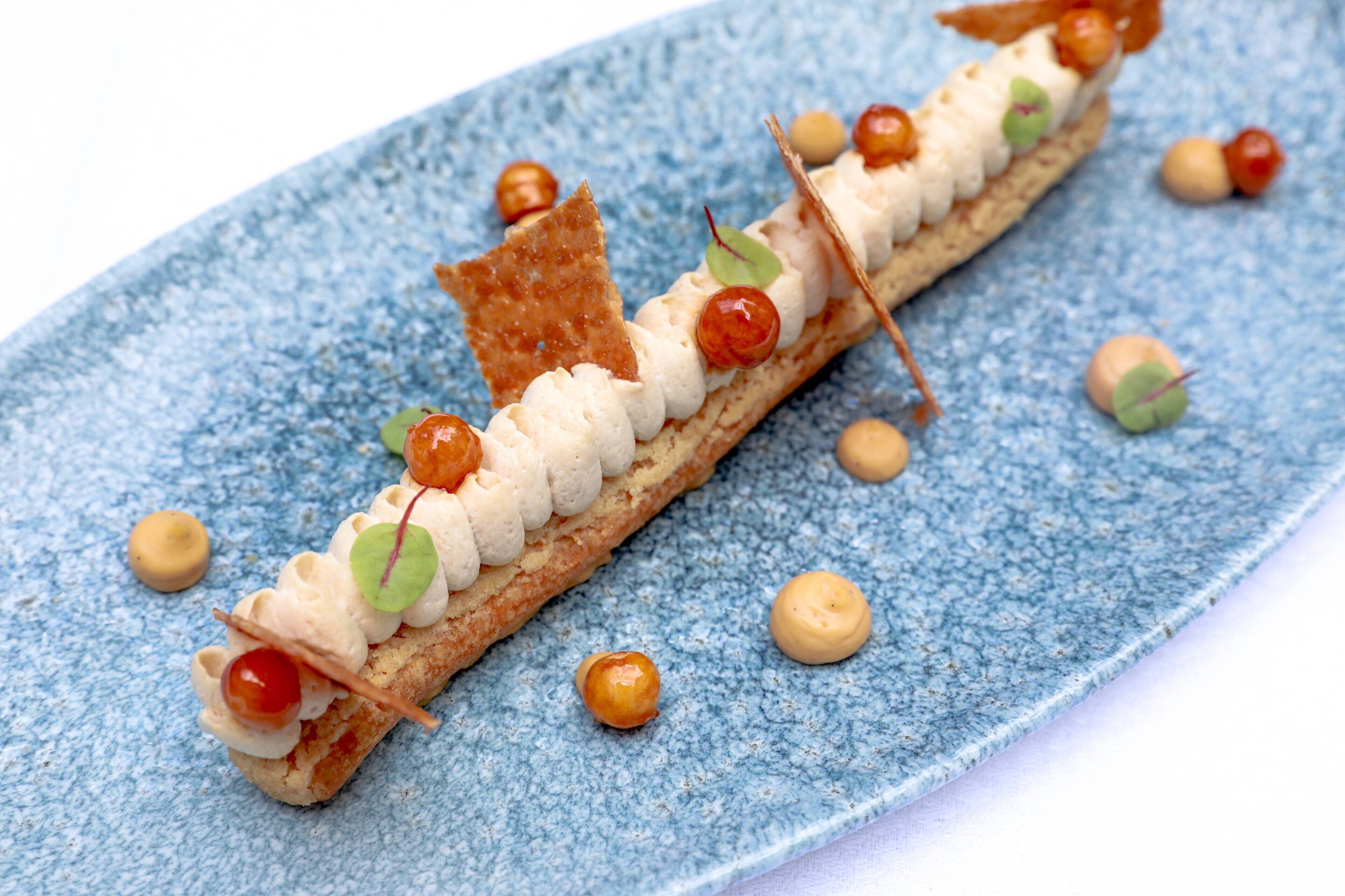 Ein Dessert auf einem blauen Teller mit strukturierter Oberfläche und verschiedenen Verzierungen.