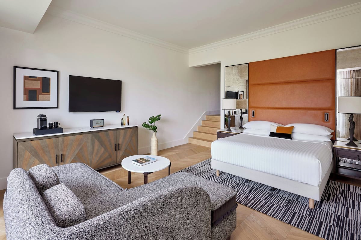 A modern hotel room with a large bed, a sofa, a small table, and a TV.