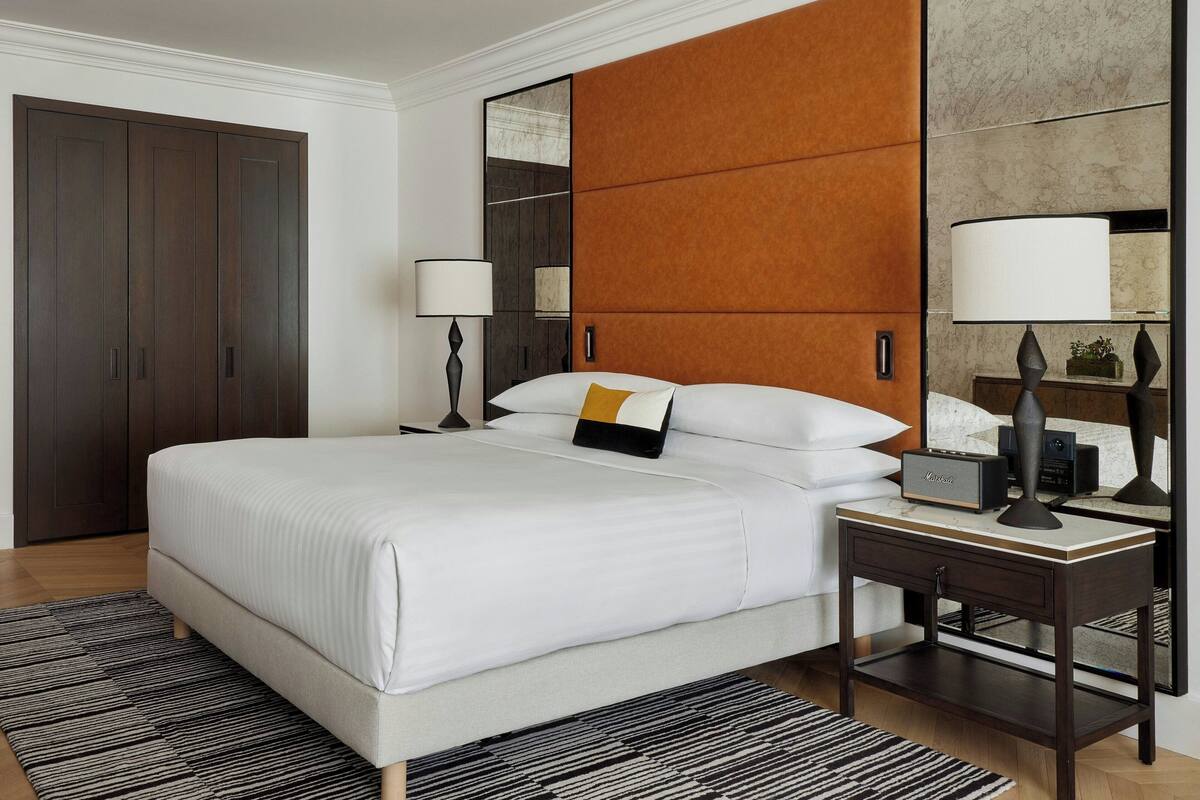 A hotel room with a large bed, two bedside tables with lamps, a mirror, and a wardrobe.