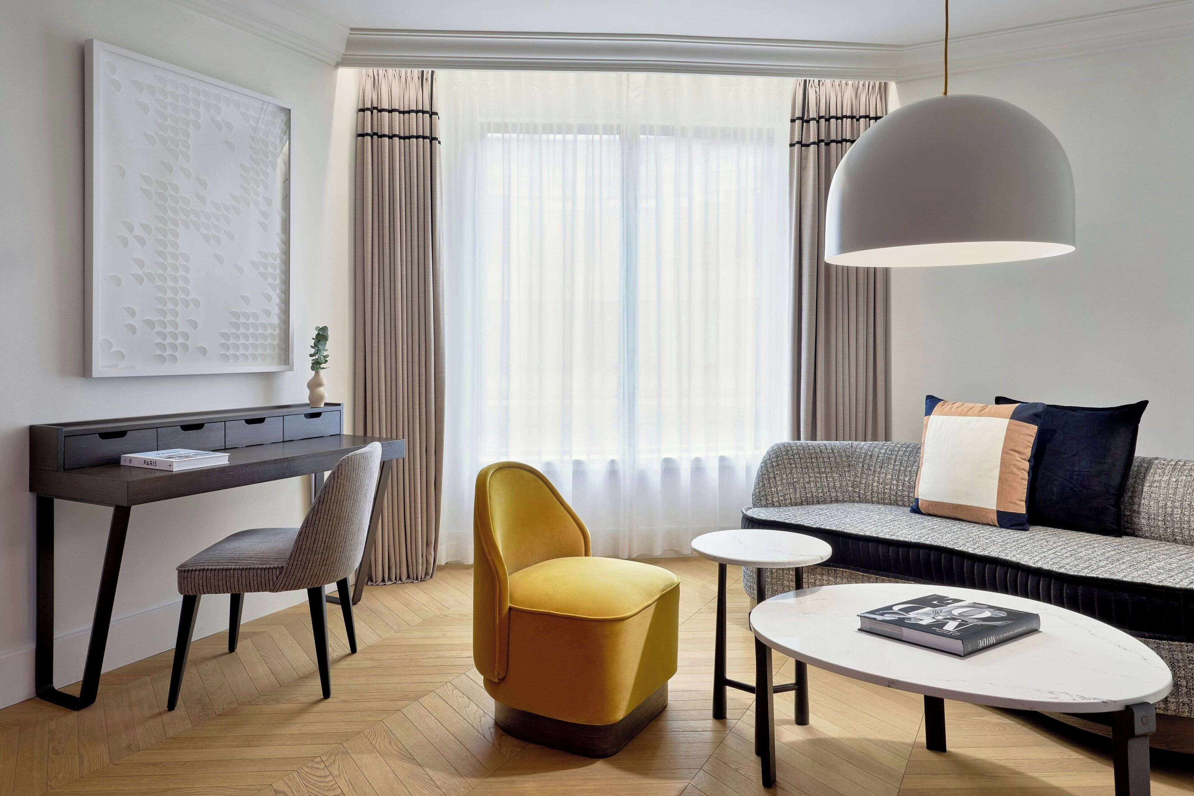 Una sala de estar moderna con un sofá, un sillón amarillo, una mesita y un escritorio con una computadora.