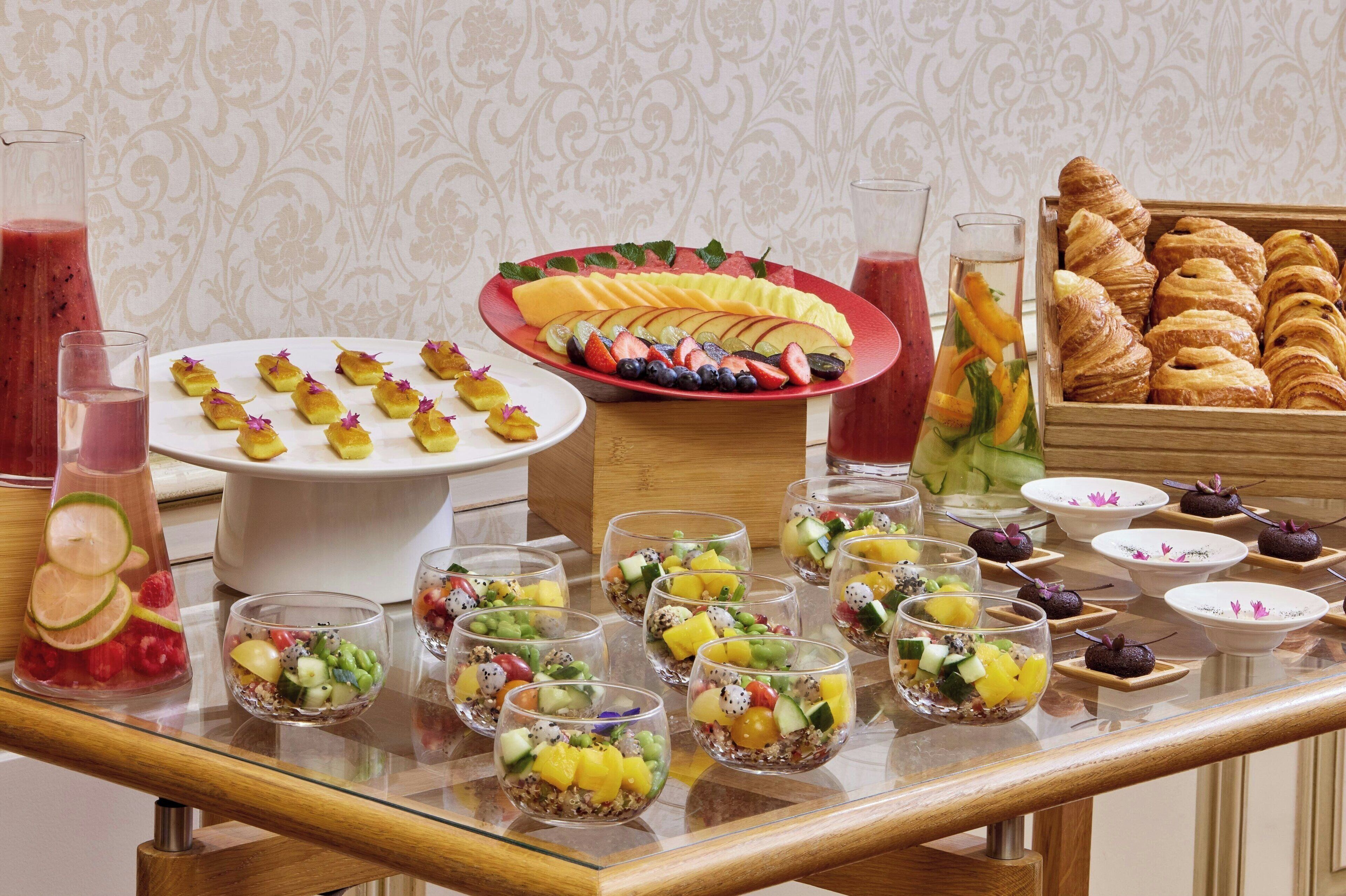 A buffet table with various food items including fruits, pastries, and beverages.