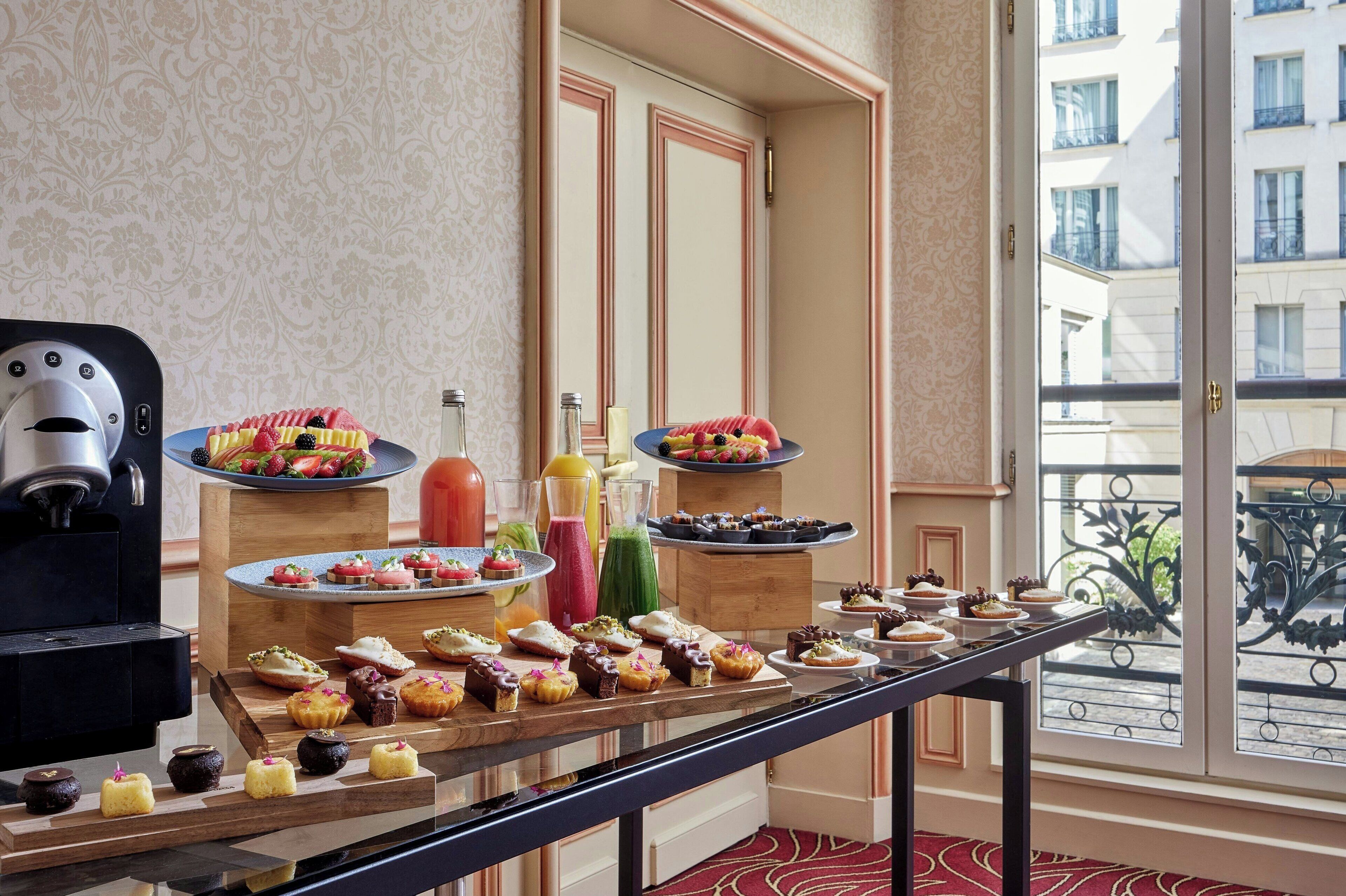 Una mesa de buffet con diversos pasteles y postres, una máquina de café y dispensadores de jugo.