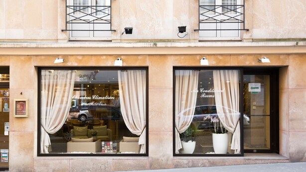 Fachada de hotel con amplias ventanas, cortinas y un letrero que indica 'Chambres Climatisées' y 'Rooms'.
