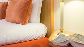 A neatly made bed with white and orange bedding, a wooden headboard, and a bedside table with a lamp and a book.