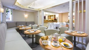 Un comedor de hotel con mesas redondas, asientos acolchados y alimentos para el desayuno.