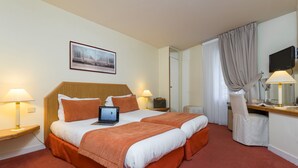 Una cama doble con una computadora portátil, dos mesitas de noche con lámparas, un televisor y un escritorio con una silla.