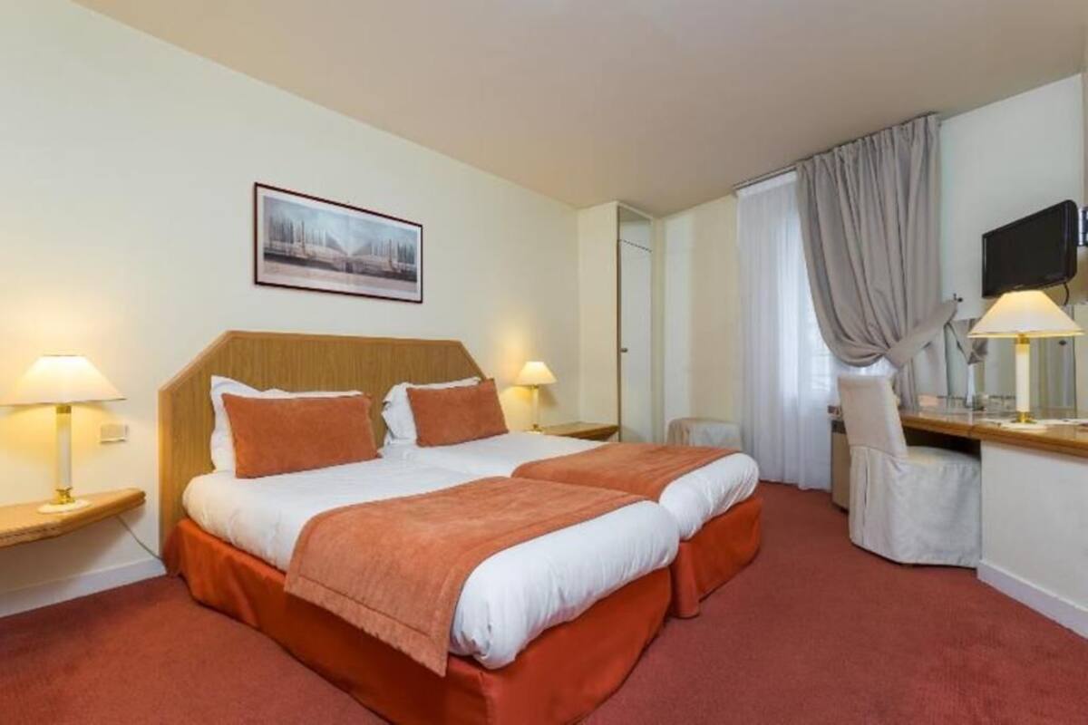 A hotel room with a double bed, two bedside tables with lamps, a desk with a chair, a television, and a framed picture on the wall.