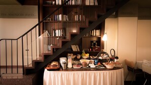 A breakfast buffet with a variety of food items and a staircase with bookshelves in the background. - Hotel Quartier Latin (Paris)