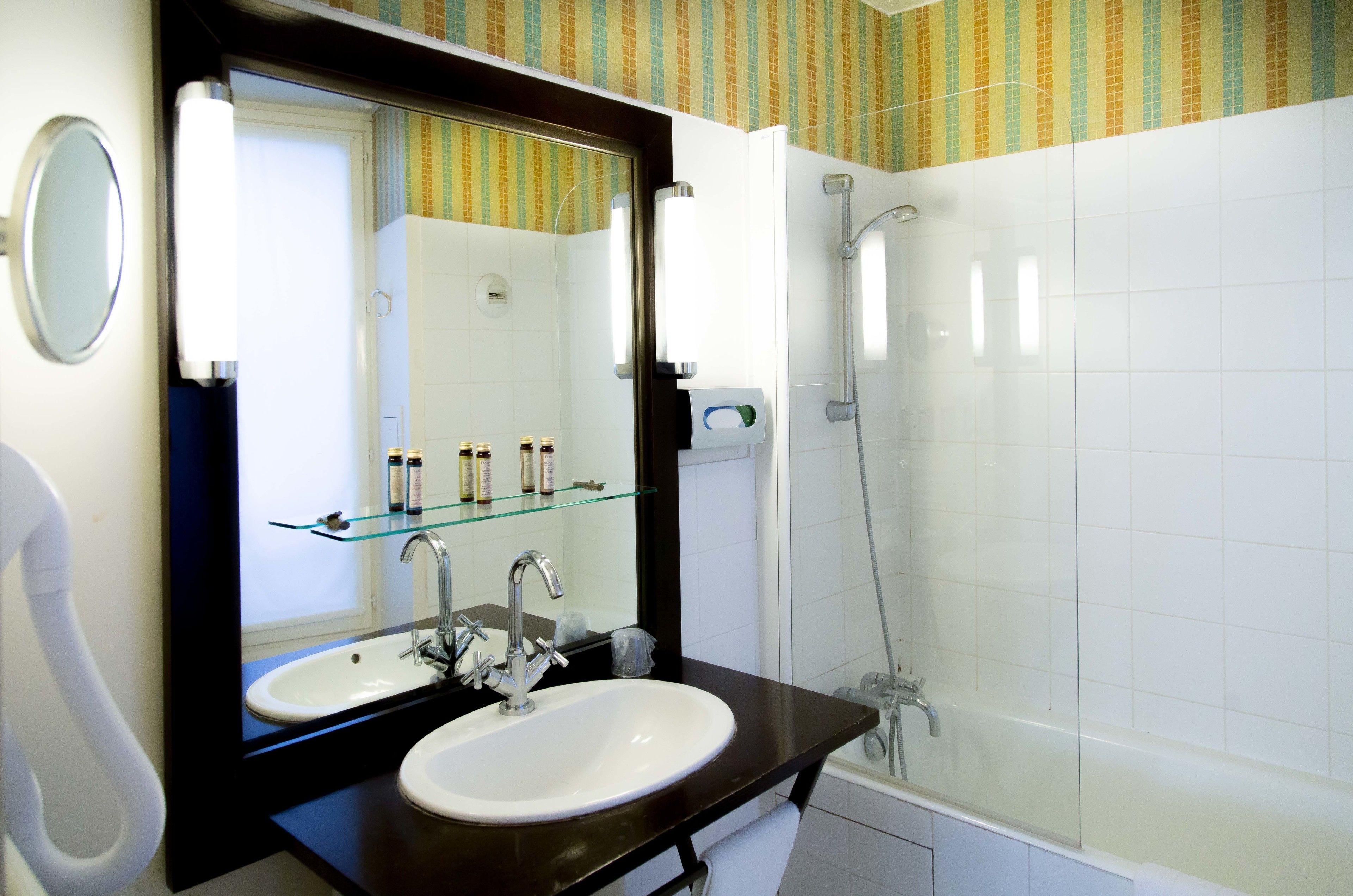 A bathroom with a white sink, dark countertop, and a glass shelf with toiletries.