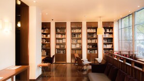 A modern library with wooden bookshelves, a reading area with a sofa, and a chess table. - Hotel Quartier Latin (Paris)