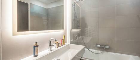 A modern bathroom with a large mirror, a white sink, and a glass-enclosed shower.