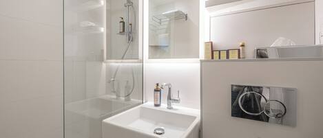 A modern bathroom with a glass-enclosed shower, a white sink, and a mirror with a towel rack.