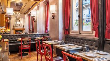 Un restaurante con una zona de asientos en una cabina de cuero negro, sillas rojas y mesas de madera.