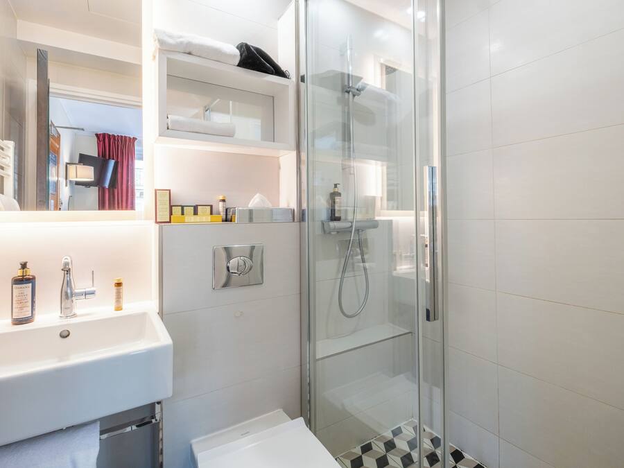 A modern bathroom with a glass-enclosed shower, a white sink with toiletries, and a mirror above the sink.