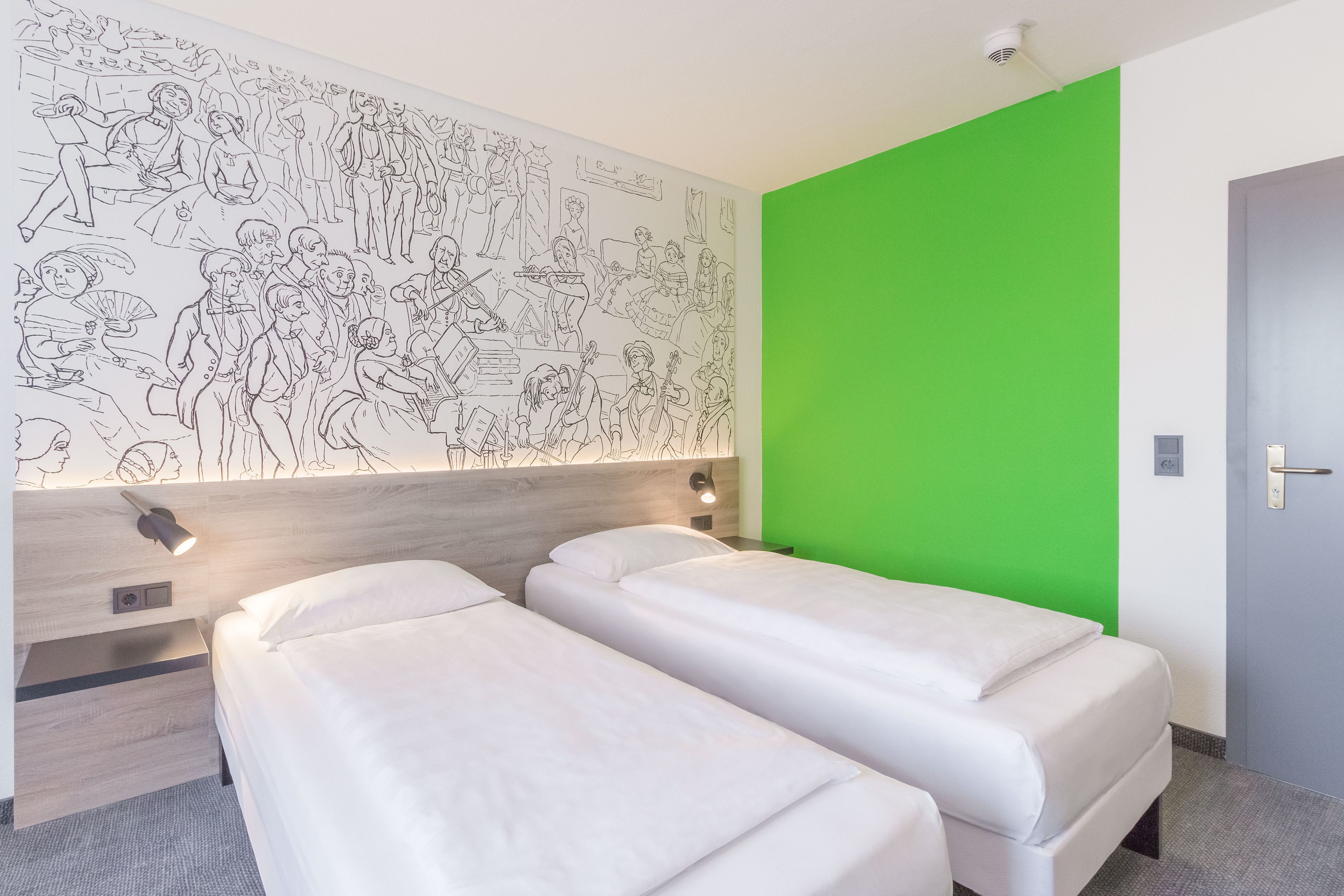Ett hotellrum med två sängar, en grön accentvägg och en väggmålning som föreställer människor.