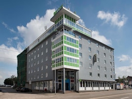 Un hotel de varios pisos con una fachada destacada en verde y blanco, amplias ventanas y una entrada visible.