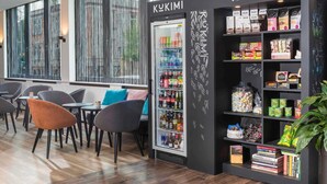 A modern café interior with a black counter, seating area, and a variety of snacks and beverages. - ibis Styles Halle (Halle (Saale))