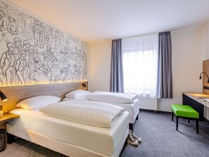 Two single beds with white linens and a wooden headboard, set against a vibrant wall mural.