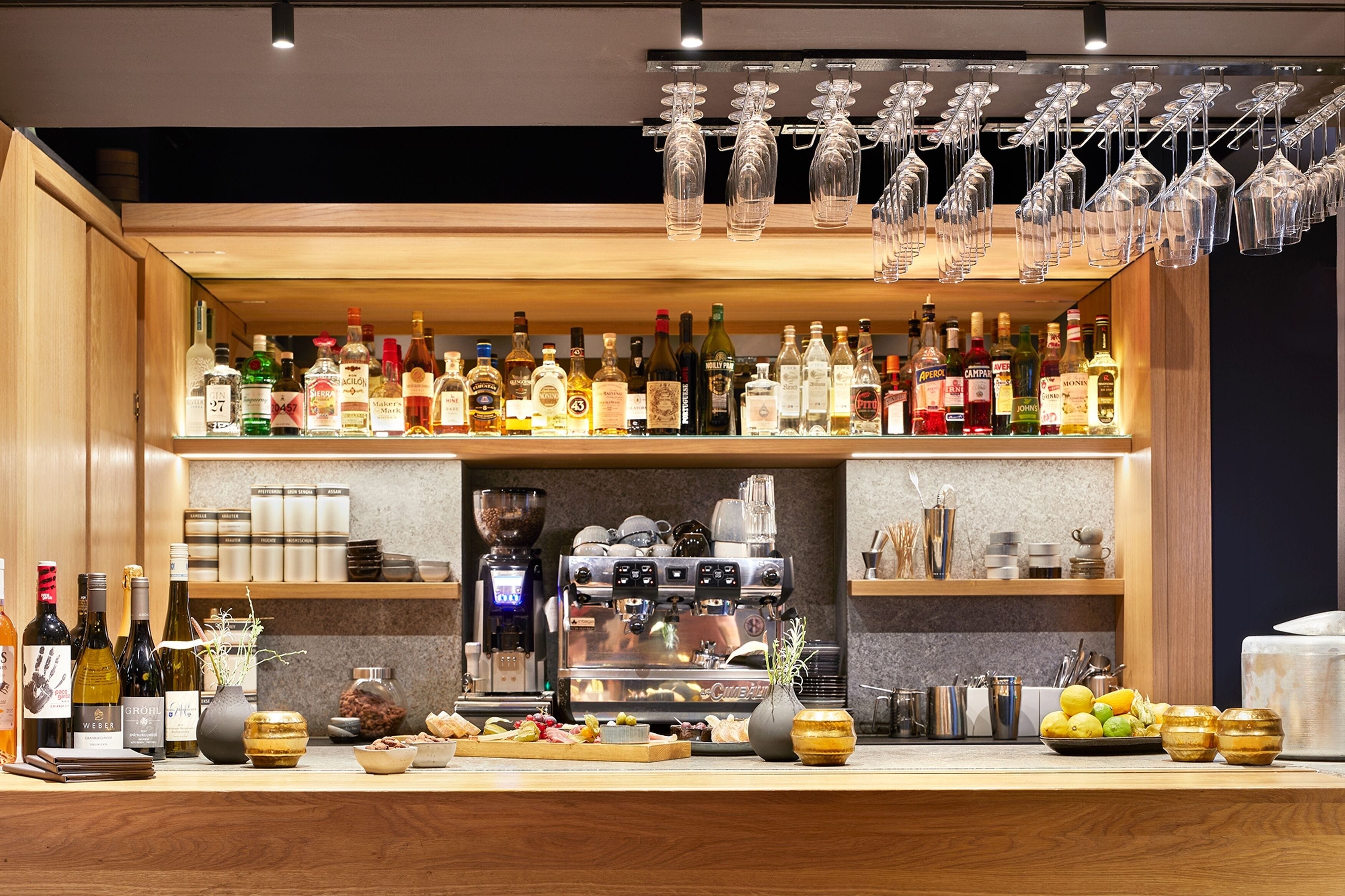Zona de bar con estantes llenos de botellas de licor, una máquina de café y diferentes utensilios de bar.