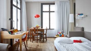 Ein Hotelzimmer mit Holzschreibtisch, Stühlen, einem Bett, einem Nachttisch und einem Fenster mit Vorhängen.