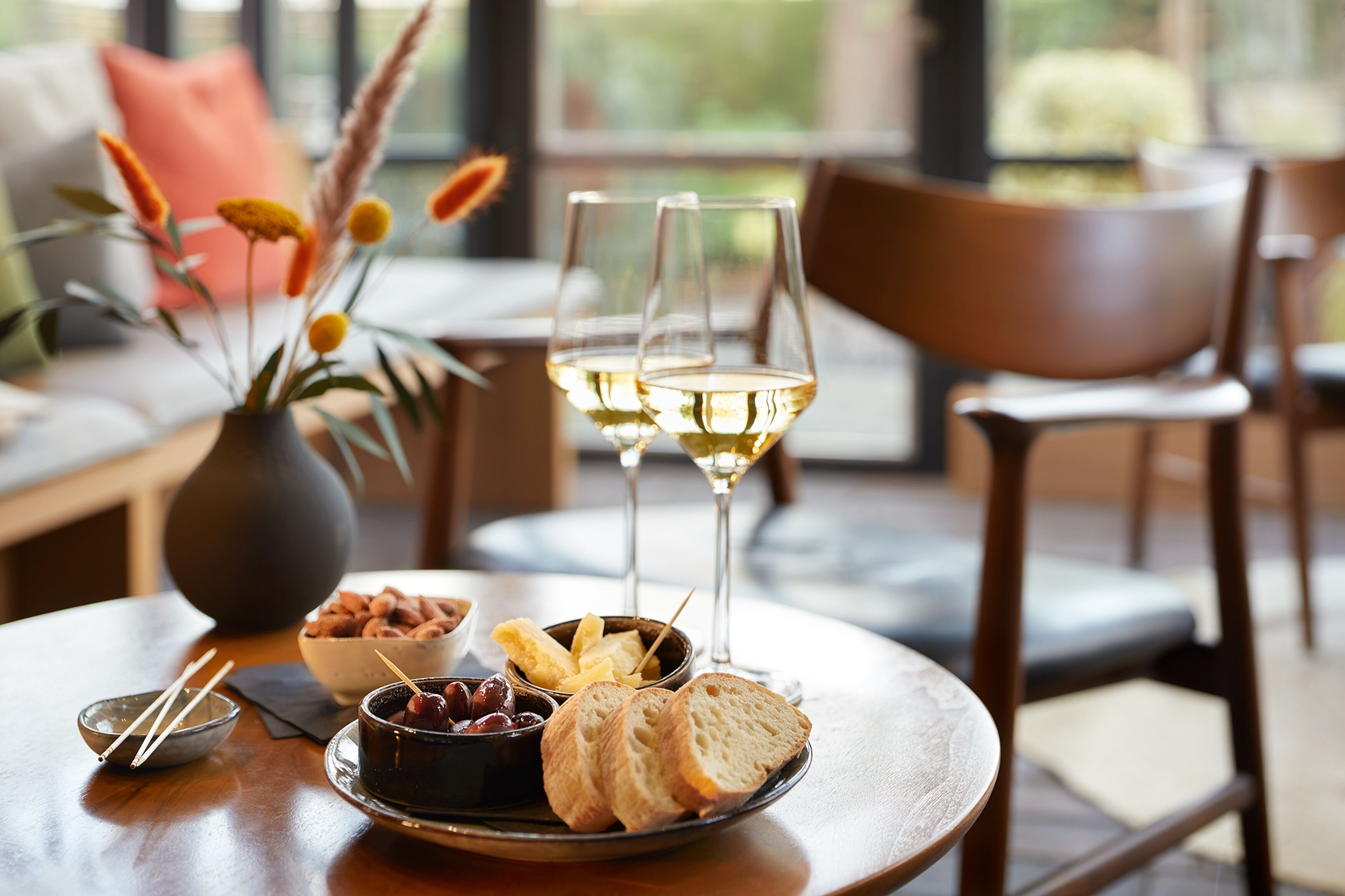 A dining table with a plate of bread, a bowl of olives, and two glasses of white wine.