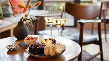 A dining table with a plate of bread, a bowl of olives, and two glasses of white wine.
