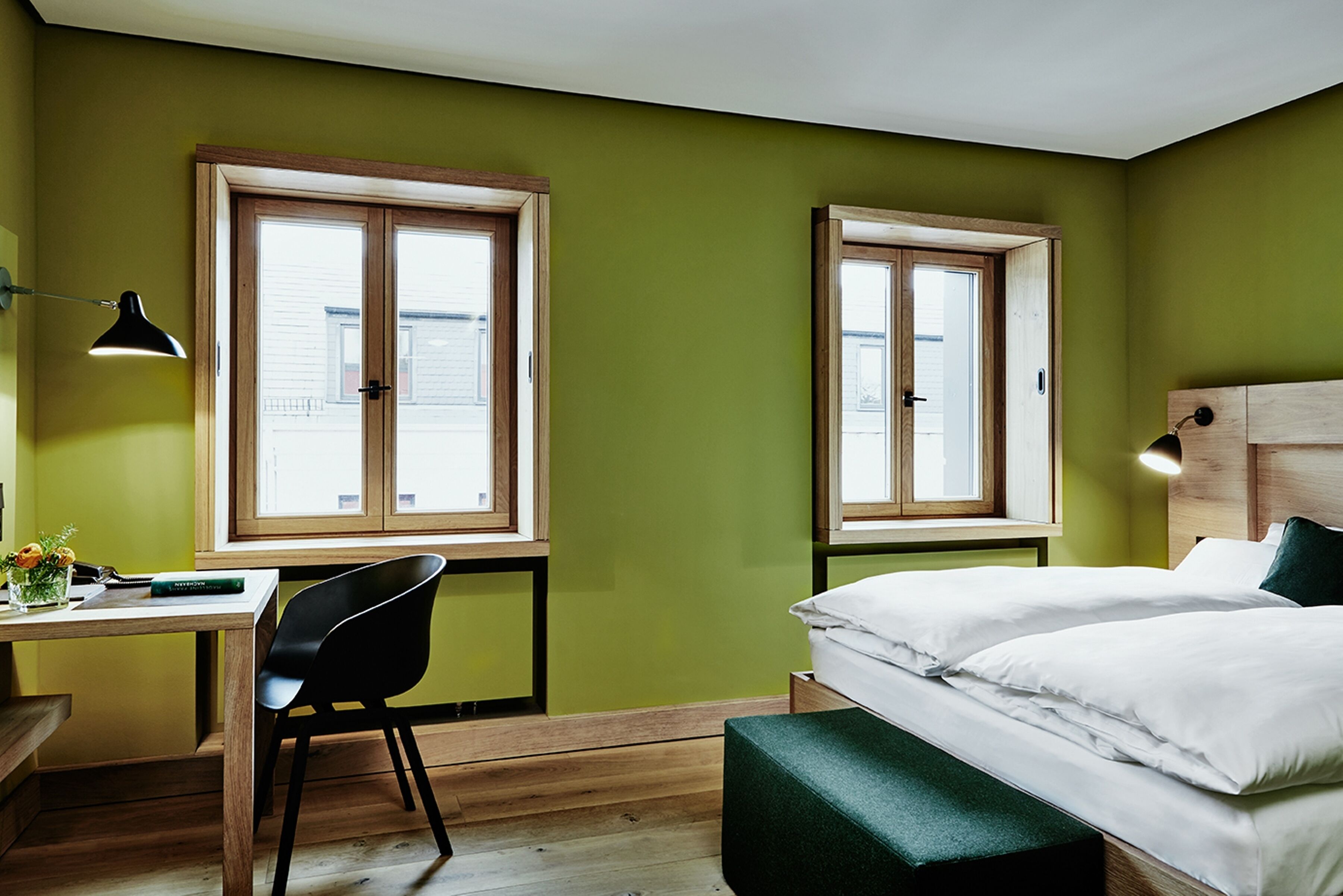 A room with two windows, a desk with a chair, and a bed with pillows.