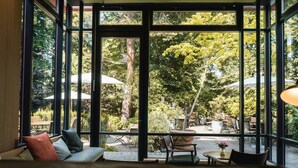 Ein Zimmer mit großen Fenstern, einem Bett, einer Couch und einer Essecke mit Gartenmöbeln.