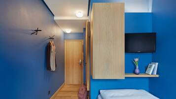 Un dormitorio moderno con una cama, un televisor montado en la pared, un armario de madera y un pasillo que conduce a una puerta.