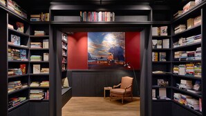 Eine Bibliothek mit Bücherregalen an beiden Seiten, einem Holzboden, einer roten Wand mit einem Gemälde und einem Stuhl in der Mitte.