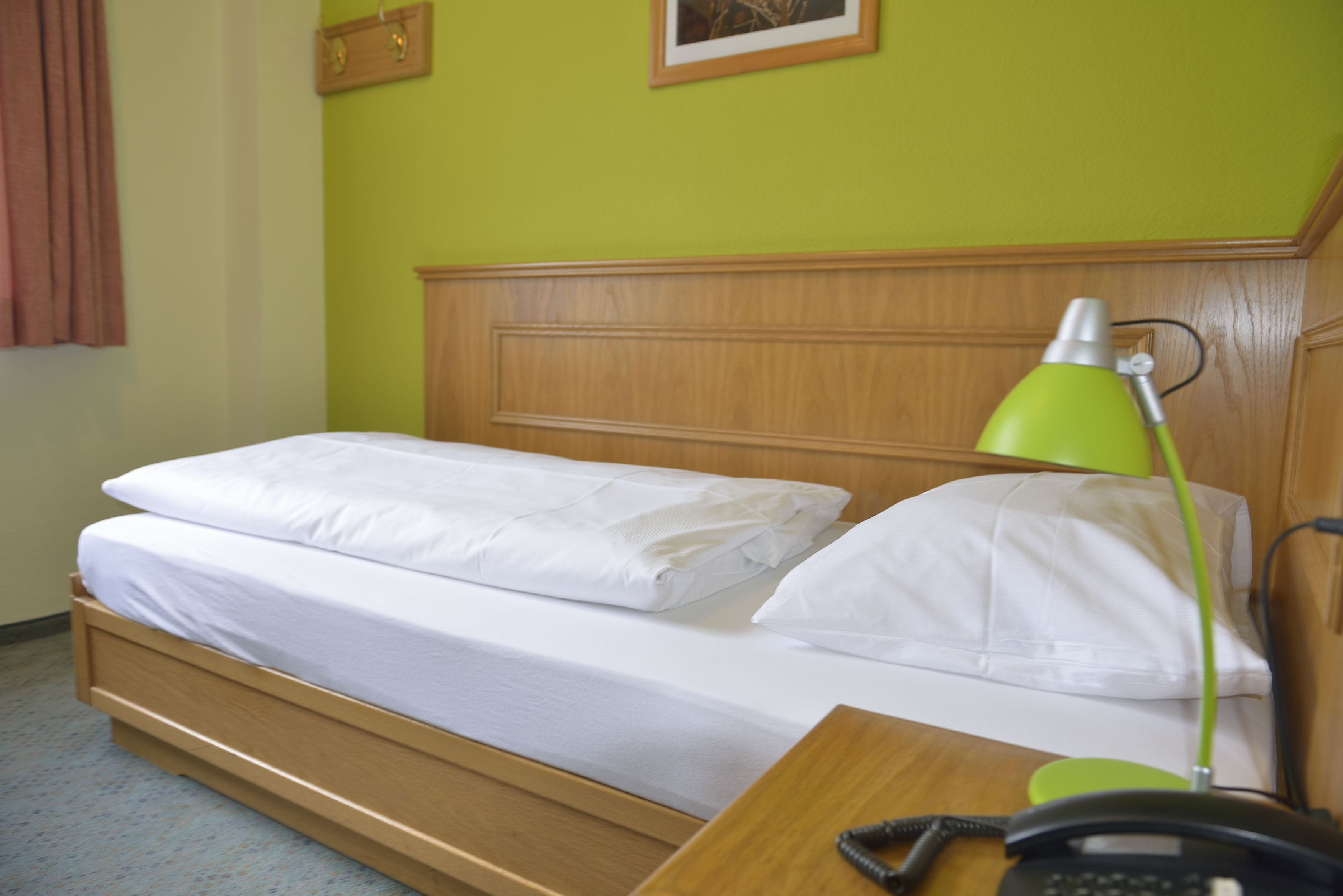 A single bed with white bedding, a wooden headboard, a green desk lamp, and a telephone on the bedside table.