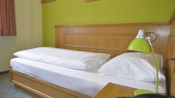 A single bed with white bedding, a wooden headboard, a green desk lamp, and a telephone on the bedside table.