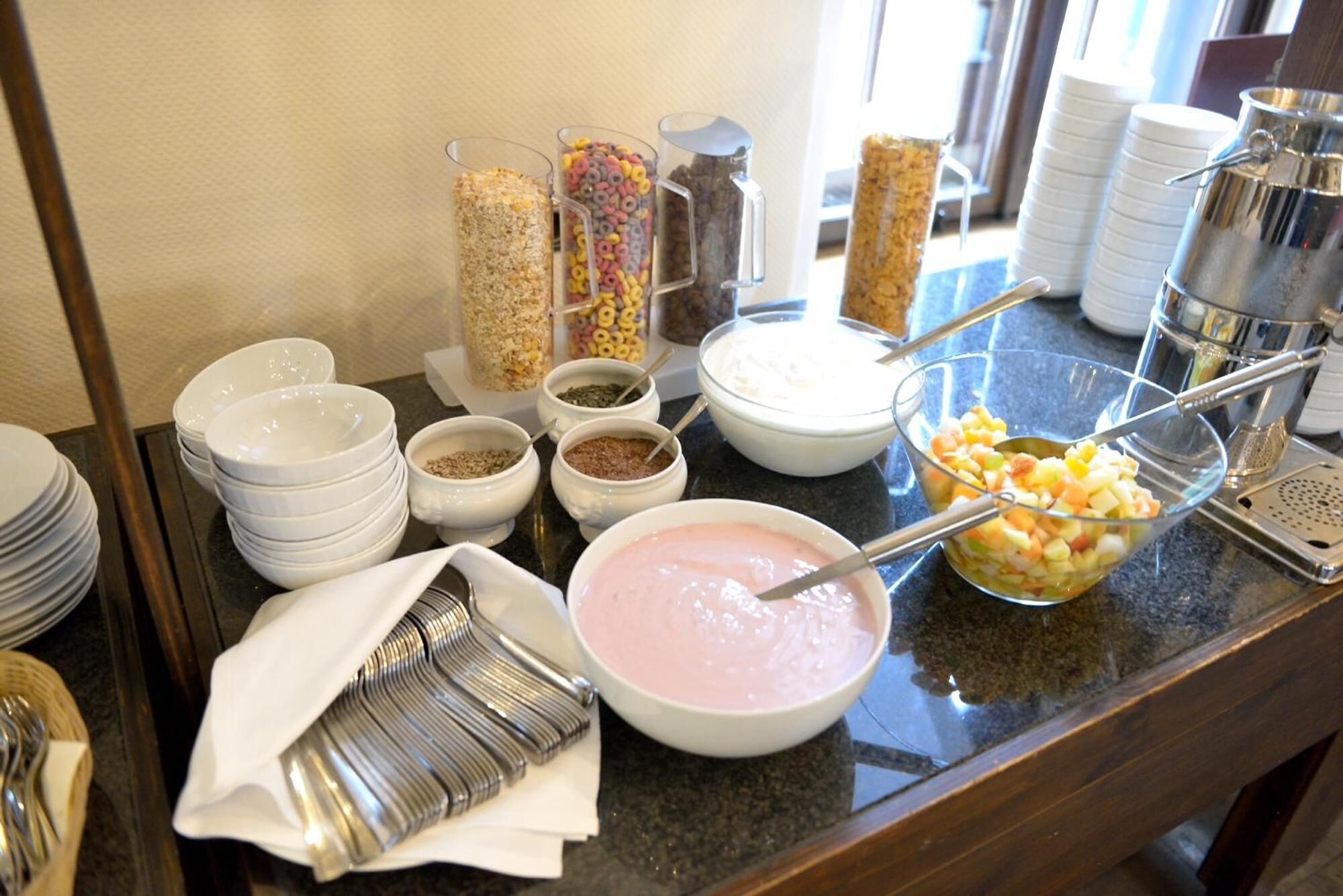 Una mesa de buffet con diversos alimentos, como cereales, yogur y fruta.