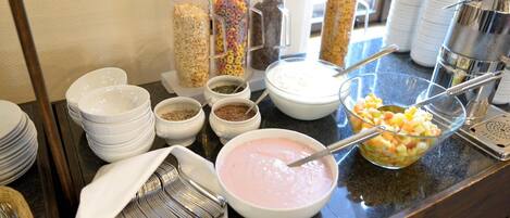 Una mesa de buffet con diversos alimentos, como cereales, yogur y fruta.