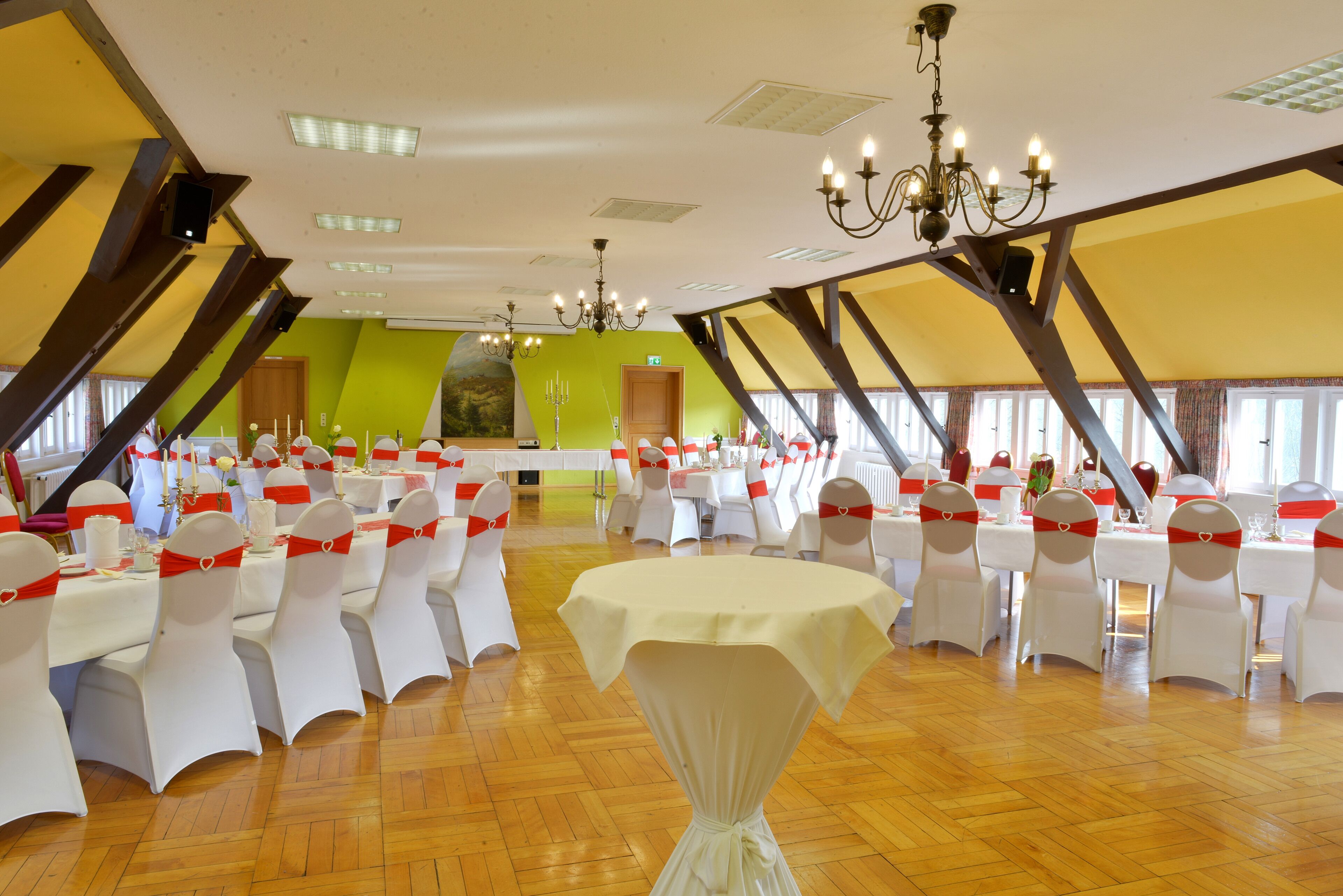 Un salón de banquetes con mesas y sillas blancas, una araña y una pared verde de acento.