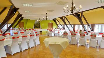 Un salón de banquetes con mesas y sillas blancas, una araña y una pared verde de acento.