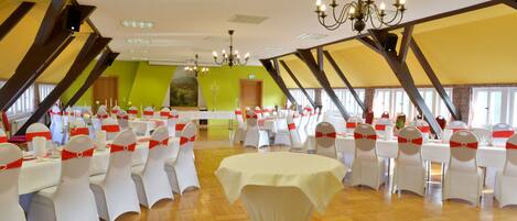 A banquet hall with white tables and chairs, a chandelier, and a green accent wall.