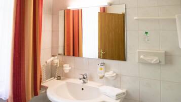 A bathroom with a white sink, mirror, towel dispenser, and a shower curtain.