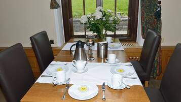 A dining table set for four with white plates, cups, and cutlery, a coffee pot, and a candle.