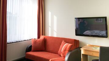 Quarto de hotel com sofá vermelho, secretária de madeira e televisão na parede.