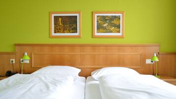 A hotel room with two beds, green walls, wooden headboard, framed pictures, and bedside lamps.