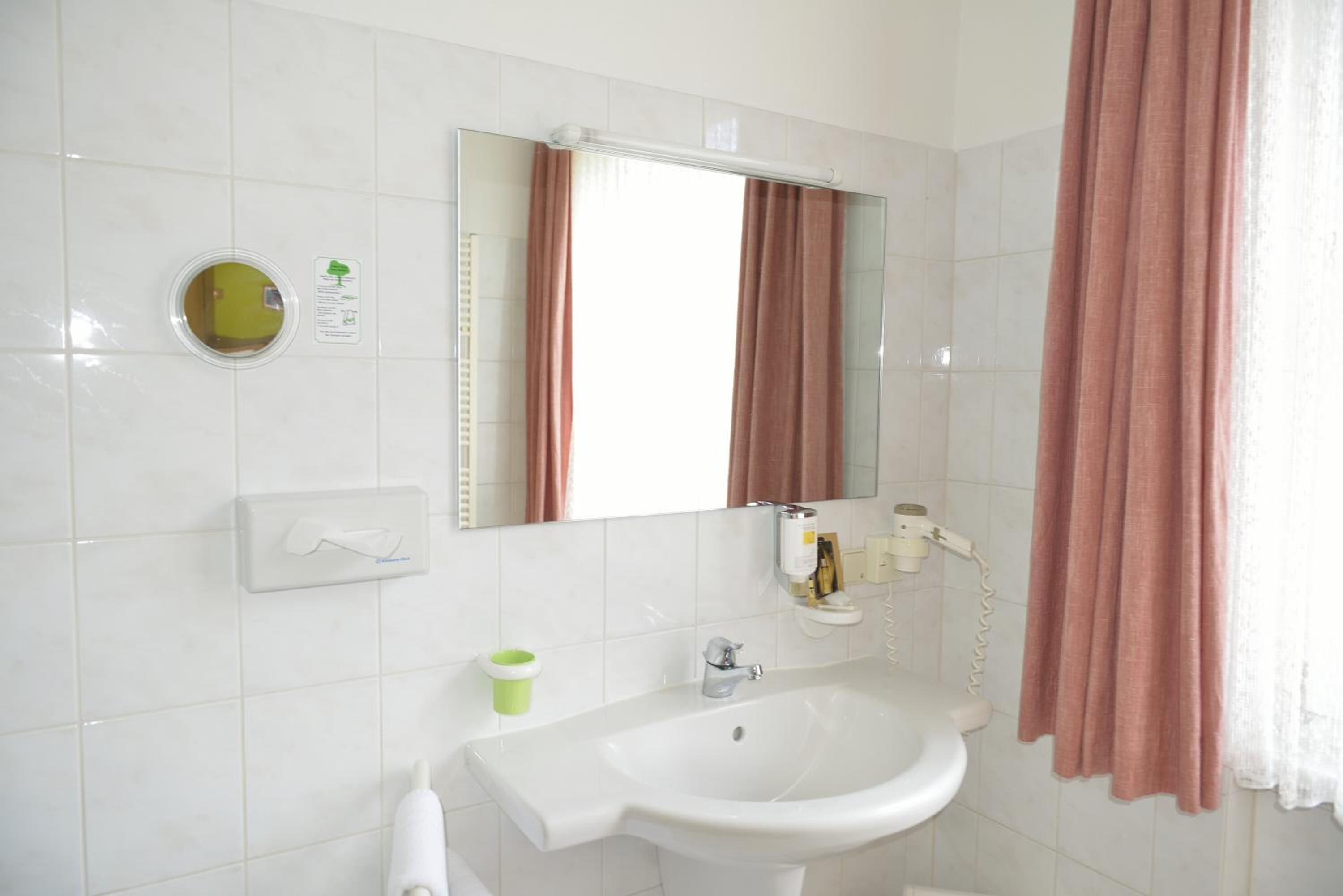 Une salle de bain avec un lavabo blanc, un miroir, un distributeur de serviettes, un porte-rouleau de papier toilette et un rideau de douche.
