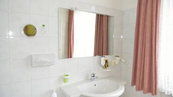 Une salle de bain avec un lavabo blanc, un miroir, un distributeur de serviettes, un porte-rouleau de papier toilette et un rideau de douche.