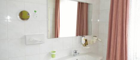 A bathroom with a white sink, a mirror, a towel dispenser, a toilet paper holder, and a shower curtain.