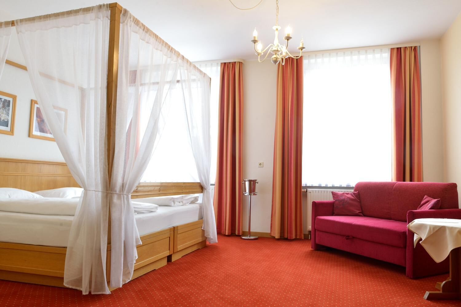 Ein Hotelzimmer mit Bett, einem roten Sofa, einer Kristallleuchter und einem Vorhangfenster.