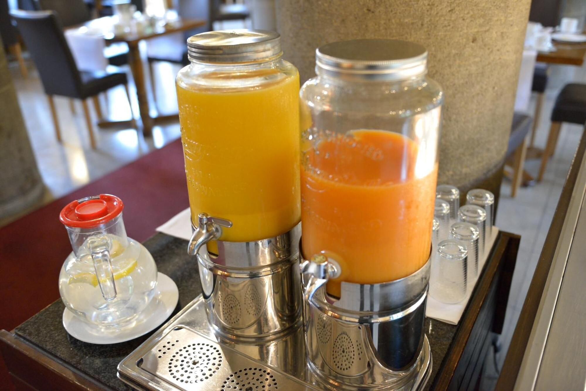 Two juice dispensers with a small pitcher of lemonade on a tray.