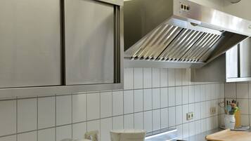A kitchen with white tiles, stainless steel appliances, and a wooden cutting board.
