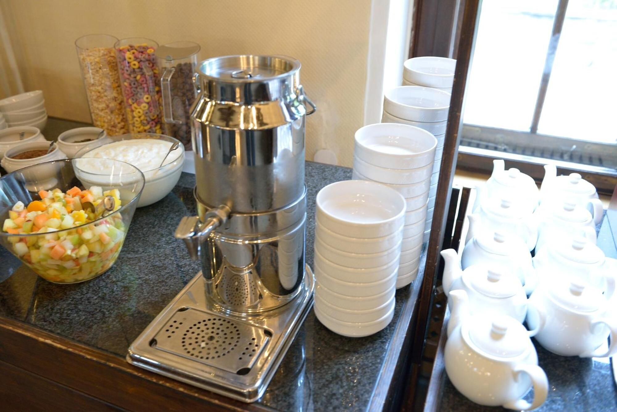 A buffet setup with a coffee maker, bowls of food, and white teapots.