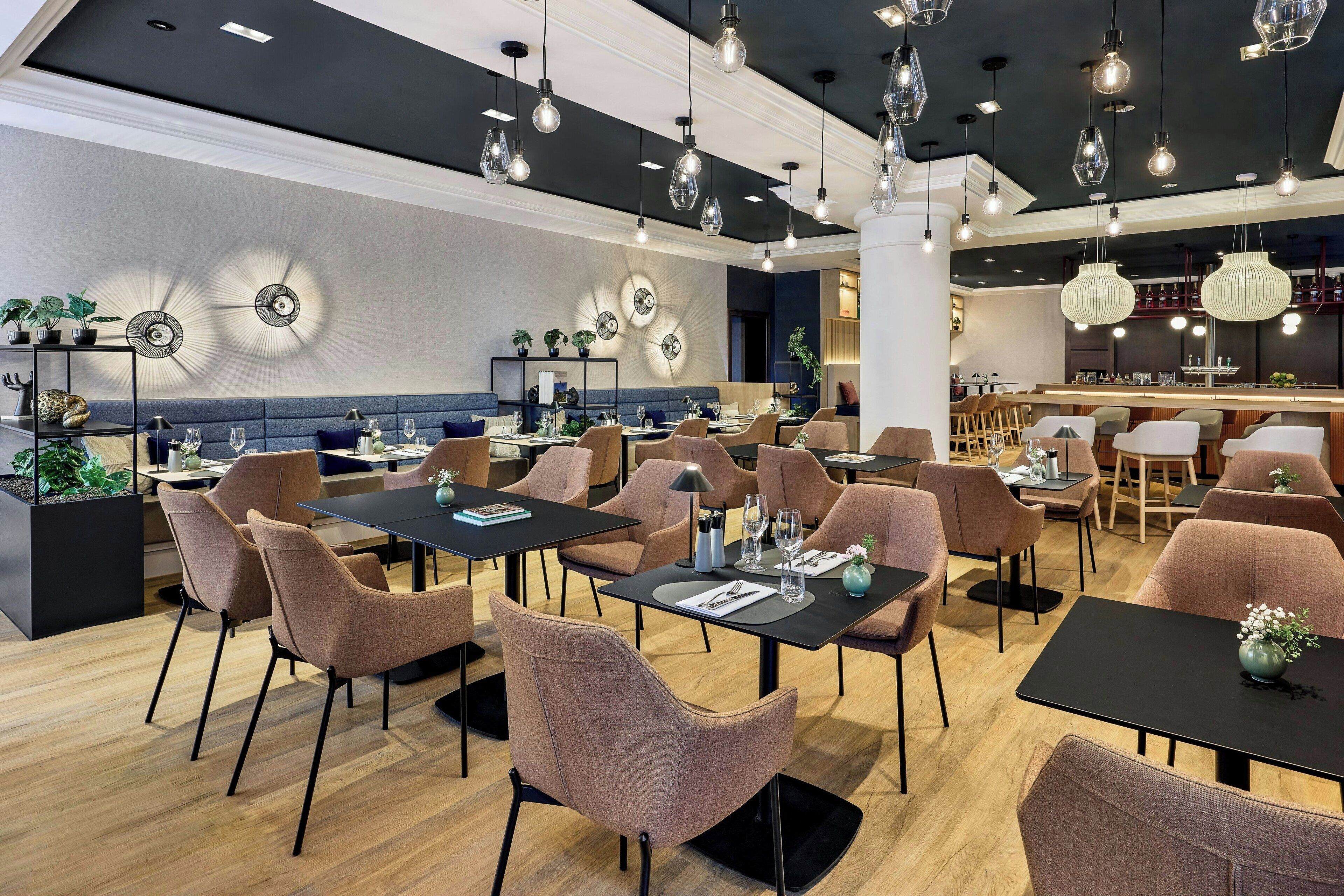 A modern restaurant interior with multiple dining tables and chairs, ambient lighting, and decorative wall elements.